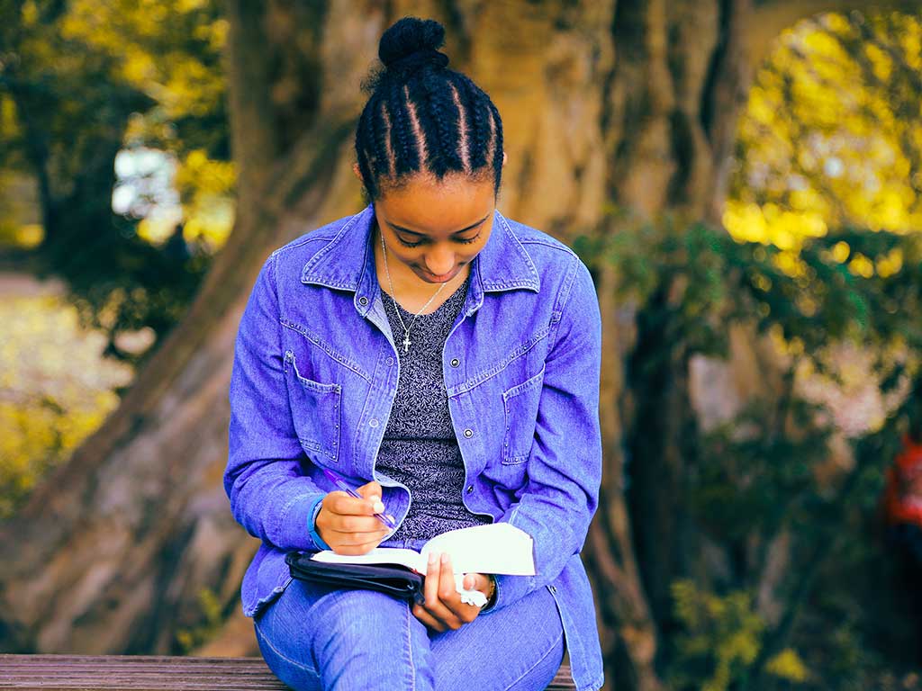 Young woman sitting on a park bench studying